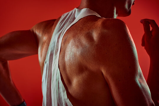 Muscular runner moving arms in red studio back closeup with vigorous effort. Activewear retail, performance coaching, sports editorial concept.