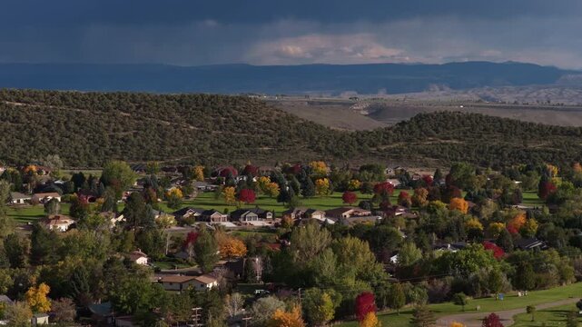 Aerial of residential neighborhood with colorful autumn foliage and rolling hills overlooking distant mountains under a stormy sky in Cedaredge Colorado under the Grand mesa