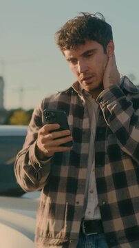Confused worried Caucasian 30s business man reading bad news on smartphone near luxury car in city disappointed stressed male sad millennial guy auto driver upset by problem loss outdoors parking lot