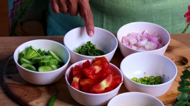Closeup of an Indian woman's finger pointing to bowls of freshly chopped vegetables during a cooking show, presenting prepared ingredients for a homemade recipe and traditional Indian meal.