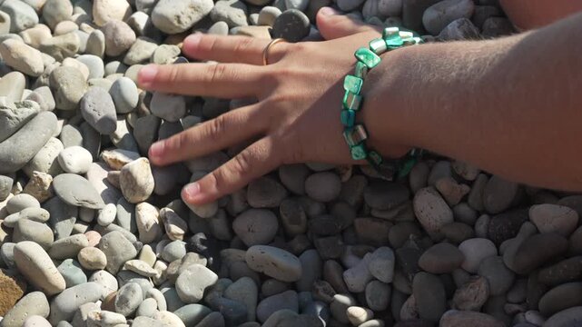 Woman playing with smooth coastal pebbles while wearing a turquoise beaded bracelet outdoors. Static close-up shot.
