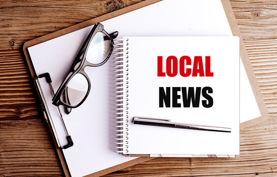 Local news text on a spiral notebook with glasses, pen and clipboard on a wooden desk, journalism and community 