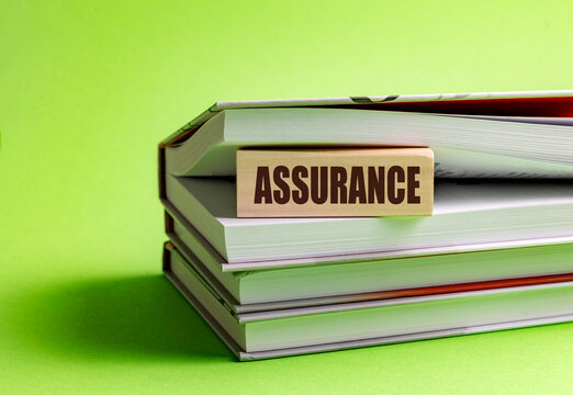 Assurance text on a wooden block between stacked books against a green background, concept of trust, confidence and quality