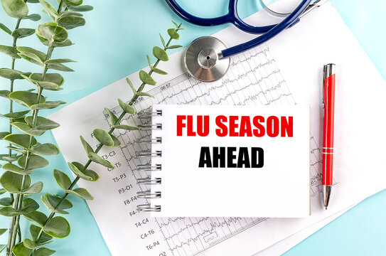 Flu season ahead text on a notebook with stethoscope, medical charts and red pen on a blue background, influenza prevention