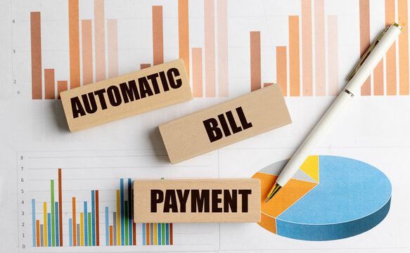 Automatic bill payment text on wooden blocks with financial charts and pen, concept of recurring payments and banking automation