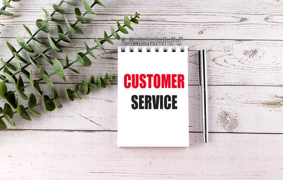 Customer service text on a spiral notebook ,pen and green leaves on a white wooden desk, business support and satisfaction concept