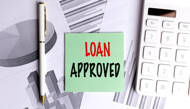Loan approved text on a green note with calculator, pen and financial charts, credit approval and financing concept