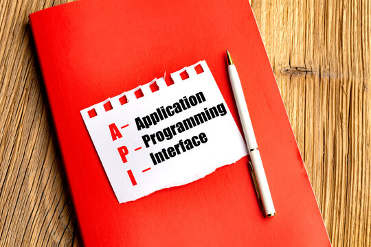 Application programming interface text on torn paper with a red notebook and pen on a wooden desk