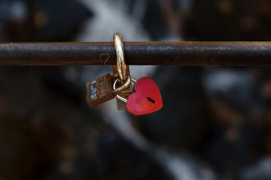 Red heart padlock linked with an old rusty lock on a metal bar. Romance, loyalty and relationship concept with copy space