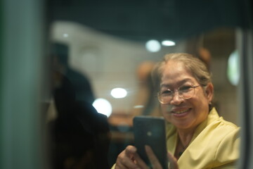 A mature woman in a yellow top smiles from her window seat on board on board a commercial flight, with her glasses catching the cabin light, good for retirement and travel themes © ultramansk