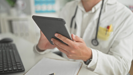 Man doctor in white coat holding tablet with both hands and tapping screen near keyboard and clipboard in building  focused care. © Krakenimages.com