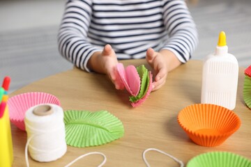Little girl making craft with paper cupcake liners at table indoors, closeup. Child creativity and art © New Africa
