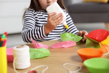 Little girl making craft with paper cupcake liners and glue at table indoors, closeup. Child creativity and art © New Africa