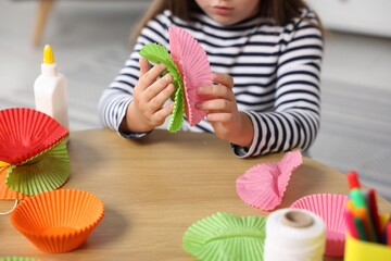 Little girl making craft with paper cupcake liners at table indoors, closeup. Child creativity and art © New Africa