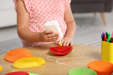 Little girl making craft with paper cupcake liners and glue at table indoors, closeup. Child creativity and art © New Africa