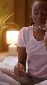 African American business woman student taking off eyeglasses rubbing eyes pain health female girl sitting bed working laptop computer writing notes learning late night education deadline home bedroom