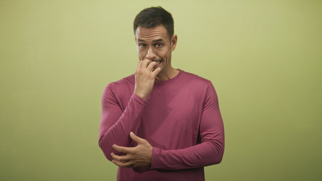 Young hispanic man with moustache wearing magenta long sleeve shirt biting nails with fingers to mouth in studio; anxiety doubt contemplation.