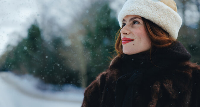 Woman looks upward at falling snow in a winter hat