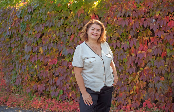 Happy plus size mature woman in her 50s smiling outdoors in an elegant classic outfit. Positive lifestyle portrait celebrating mature beauty, confidence, happiness, self acceptance and an active 55s