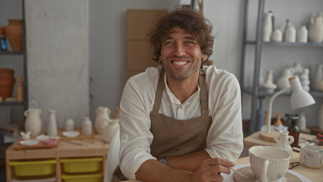Seated man in apron holding a cup and spoon at a pottery table surrounded by bisque vases and tools in an artisan studio; calm creativity.
