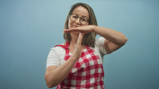 Woman wearing red check apron makes a t hand gesture while water drips between her palms in studio; household patience.