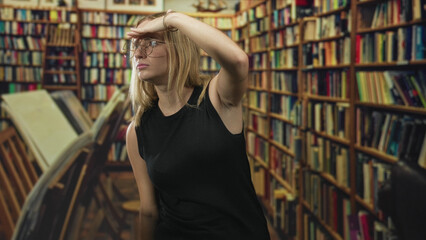 Woman shields eyes with hand while scanning tall bookshelves in a crowded library building aisle  quiet curiosity focus. © Krakenimages.com