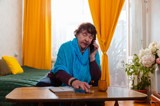 Senior female enjoying a simple dice game indoors and calls at phone. Quiet routine and comfort. Concept of aging and lifestyle.