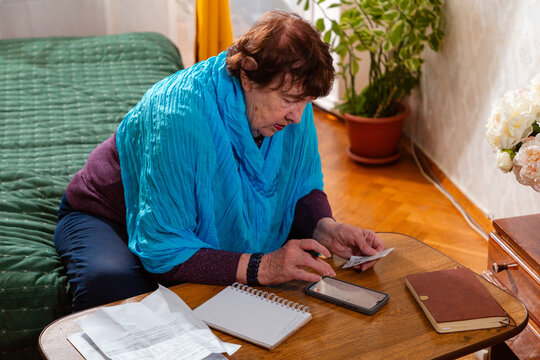 Older woman reviewing receipts and counting cash at table. Practical daily task and discipline. Concept of home accounting and savings.