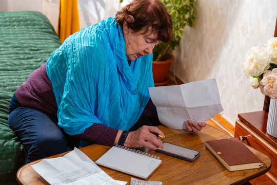 Senior woman reviewing grocery list and household expenses at home. Frugal choices and discipline. Concept of budgeting poverty.