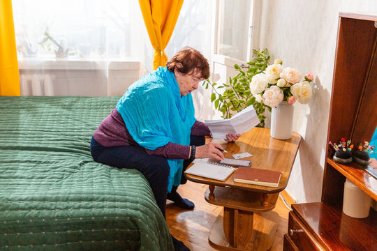 Senior female writing financial goals in notebook at home desk. Smart planning and confidence. Concept of active retirement and money care.