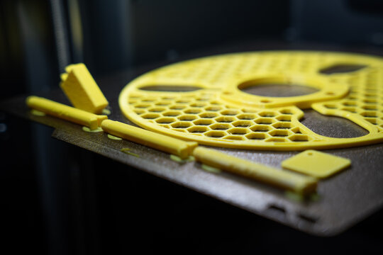 Yellow 3D printed plastic spool parts with honeycomb pattern resting on a textured build plate inside a printer chamber.