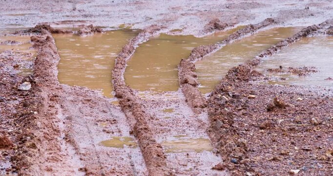 Curved parallel tire grooves cut into arid earth collect brownish water, creating linear channels across barren terrain. Overhead static shot reveals vehicle impressions in dusty landscape with