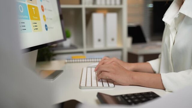 Business professional working at a computer, analyzing business data and managing office tasks using a keyboard, mouse, and calculator.