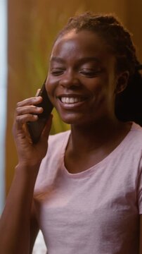 Happy African American woman talking smartphone call at home bedroom night laughing cheerful female friendly relaxed girl student working online laptop chatting conversation mobile phone telling story