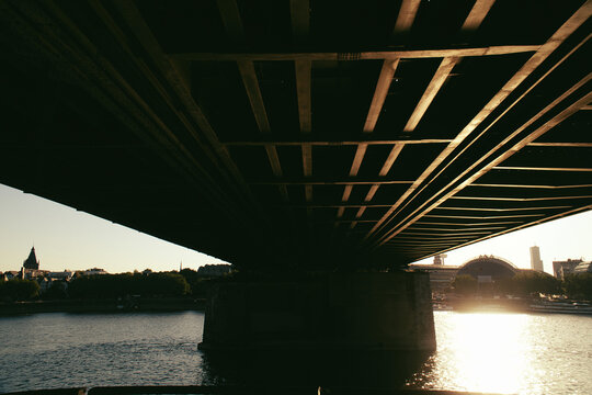 Underside of a steel bridge over a river at sunset.