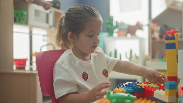 Hispanic girl stacking colorful toy blocks with hand, constructing a tower in a building; concentration learning creativity.