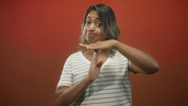 Hispanic woman showing time out hand gesture with visible hands and striped shirt in studio; dismissal boundary.