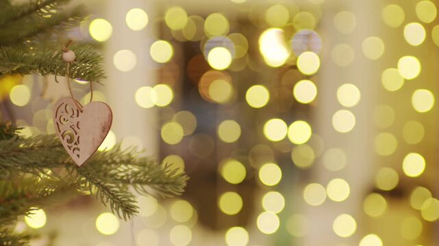 A carved wooden heart-shaped Christmas tree ornament hangs from the branch of a green fir tree. 