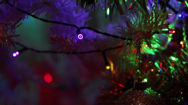 A close-up view of a white Christmas tree decorated with multicolored LED lights gently twinkling, shimmering tinsel, and Christmas ornaments.