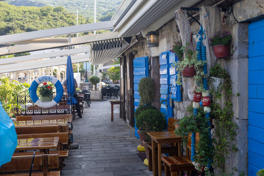 June 30, 2026, Budva, Montenegro, Charming waterfront restaurant with blue shutters, wooden tables, and vibrant plants along the pathway