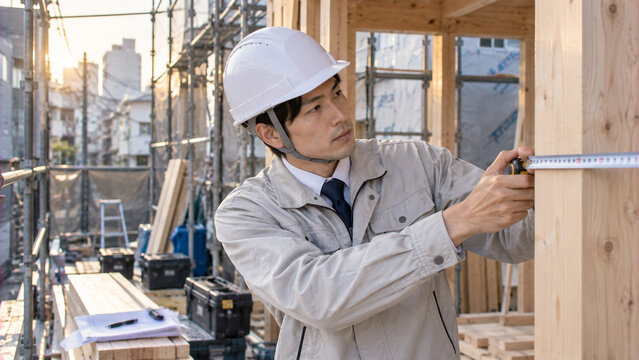 木造住宅の建築現場でメジャーを使用して柱の寸法を測定する日本人男性の施工管理技術者
