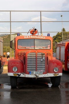 June 26, 2026, Petrovac, Montenegro, Vintage red fire truck parked near a sports court with people playing tennis under a blue sky