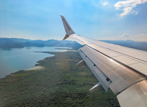 June 25, 2026, Montenegro, Airplane wing view over lush green landscape and shimmering water body under a clear blue sky