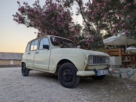 June 28, 2026, Petrovac, Montenegro, Classic vintage car parked under flowering trees near rustic building at sunset with outdoor seating