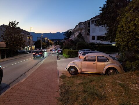 July 3, 2026, Kotor, Montenegro, Old Volkswagen Beetle parked on grass beside a quiet street at dusk with mountains in the background