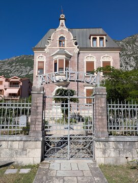 July 4, 2026, Kotor, Montenegro, Historic building with ornate gate and mountain backdrop under clear blue sky in coastal town of Angjelija