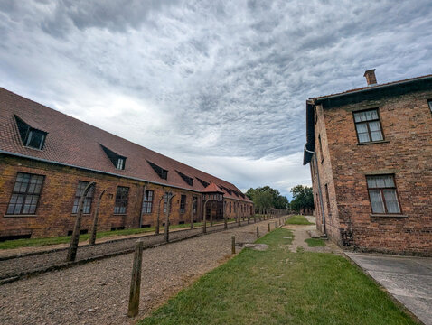 July 7, 2026, Oswiecim, Poland, Historic brick buildings and gravel pathways at a former concentration camp site with trees and a cloudy sky