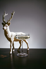 Champagne coupe with sparkling wine and decorative white reindeer figurine on dark table for Christmas celebration © ShapeImages