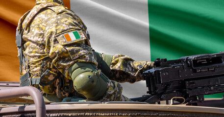 Fototapeta premium Ivory Coast flag with soldier at machine gun turret in front of it. Closeup side view.