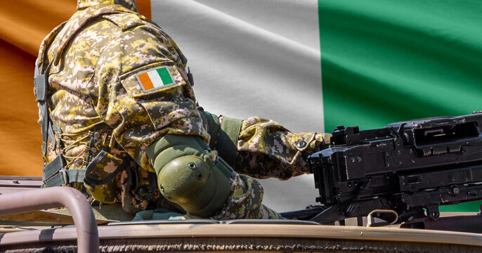 Ivory Coast flag with soldier at machine gun turret in front of it. Closeup side view.